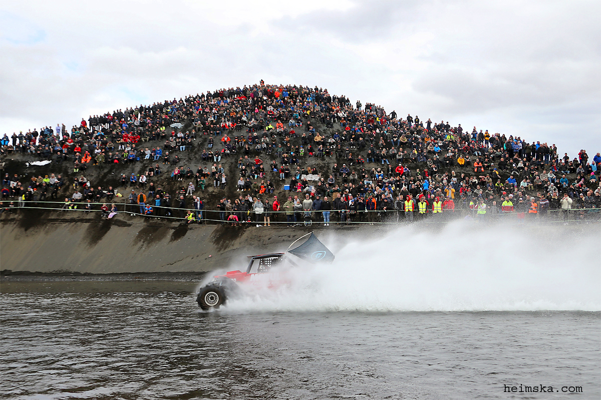 Spectator crowd lining a hillside above a torfæra water obstacle