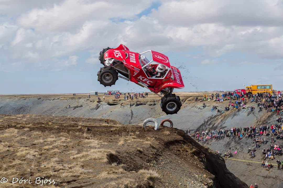 Red torfæra buggy launching off a water-filled obstacle