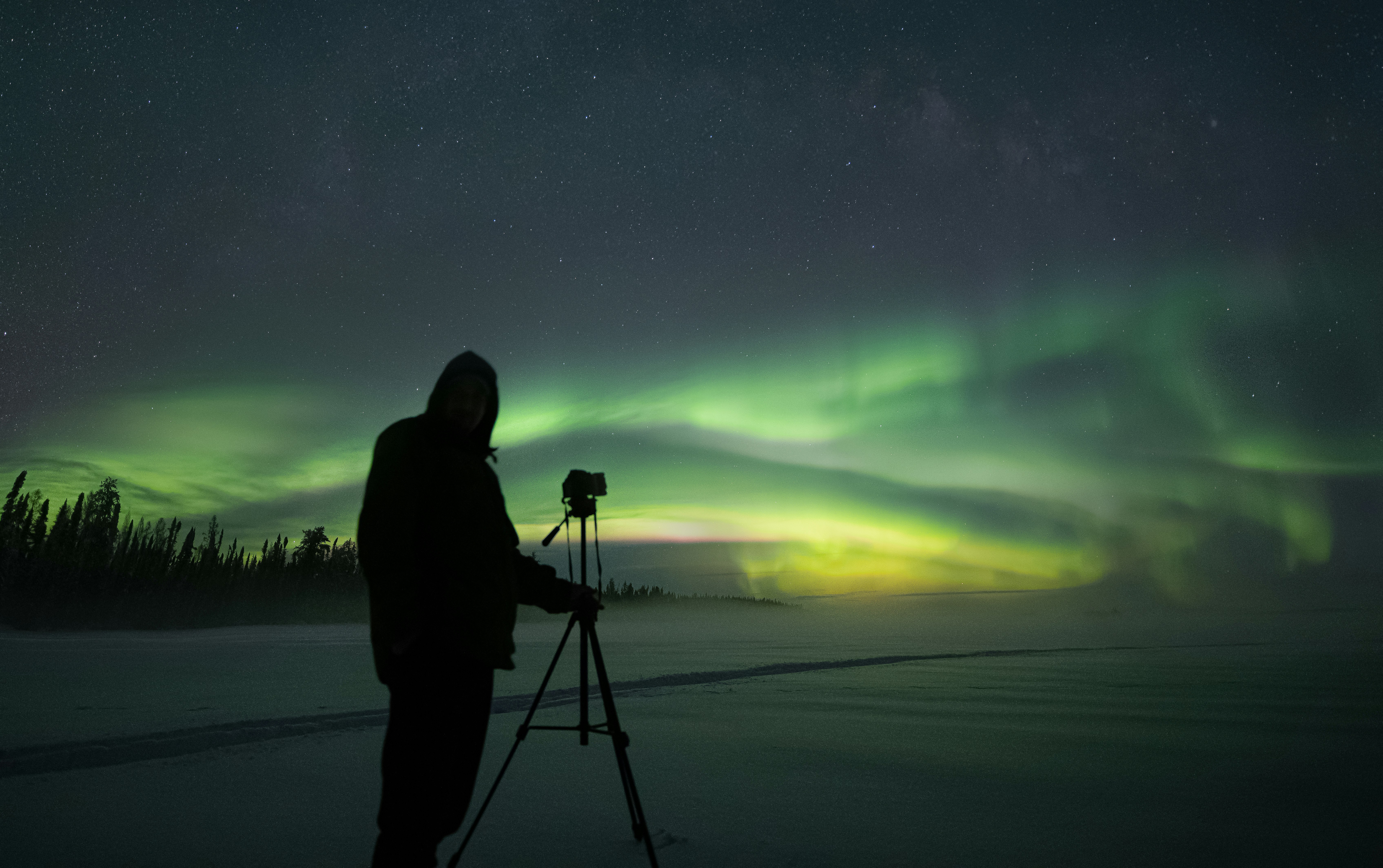 Tripod set up beside a frozen lake under northern lights
