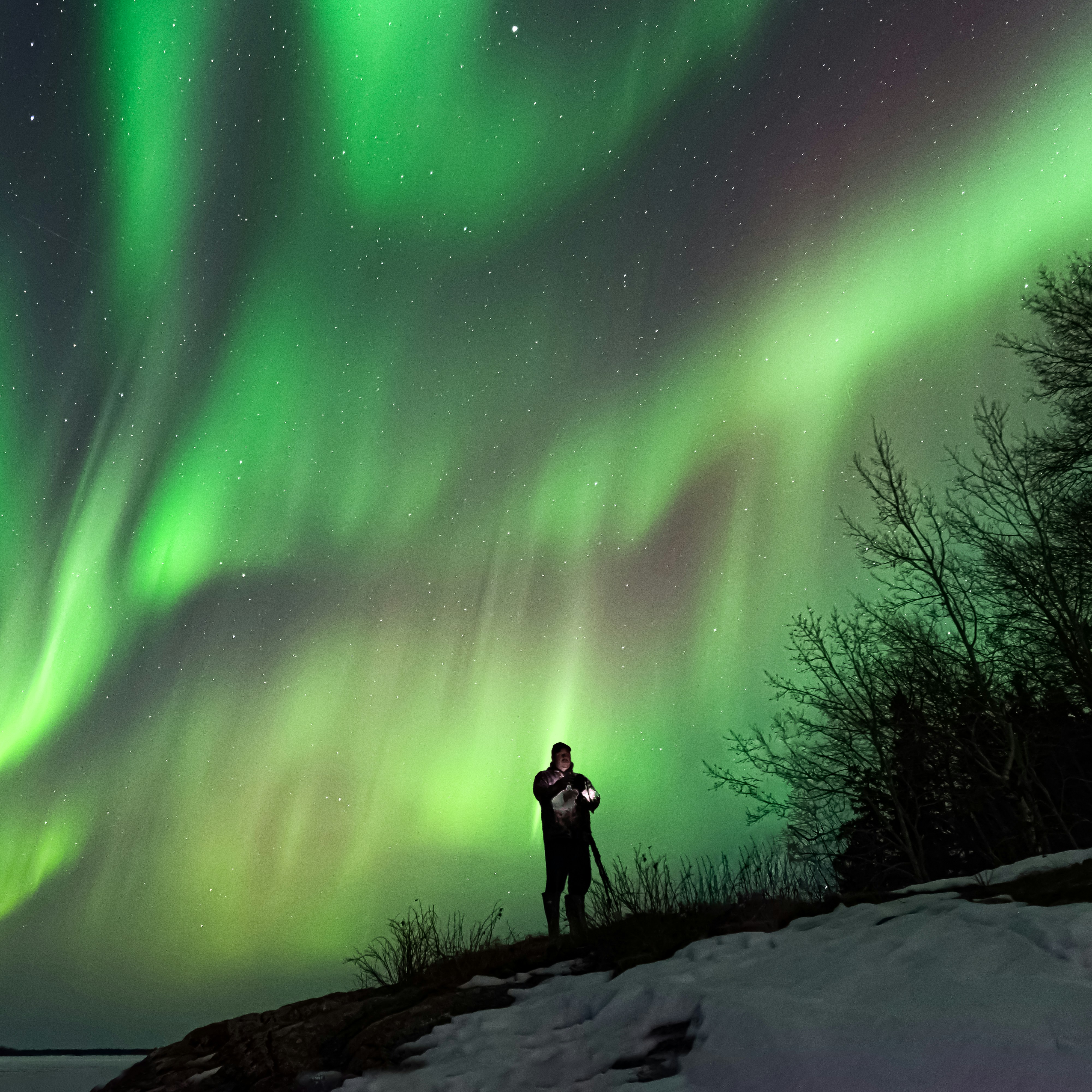 Photographer standing under strong northern lights in winter