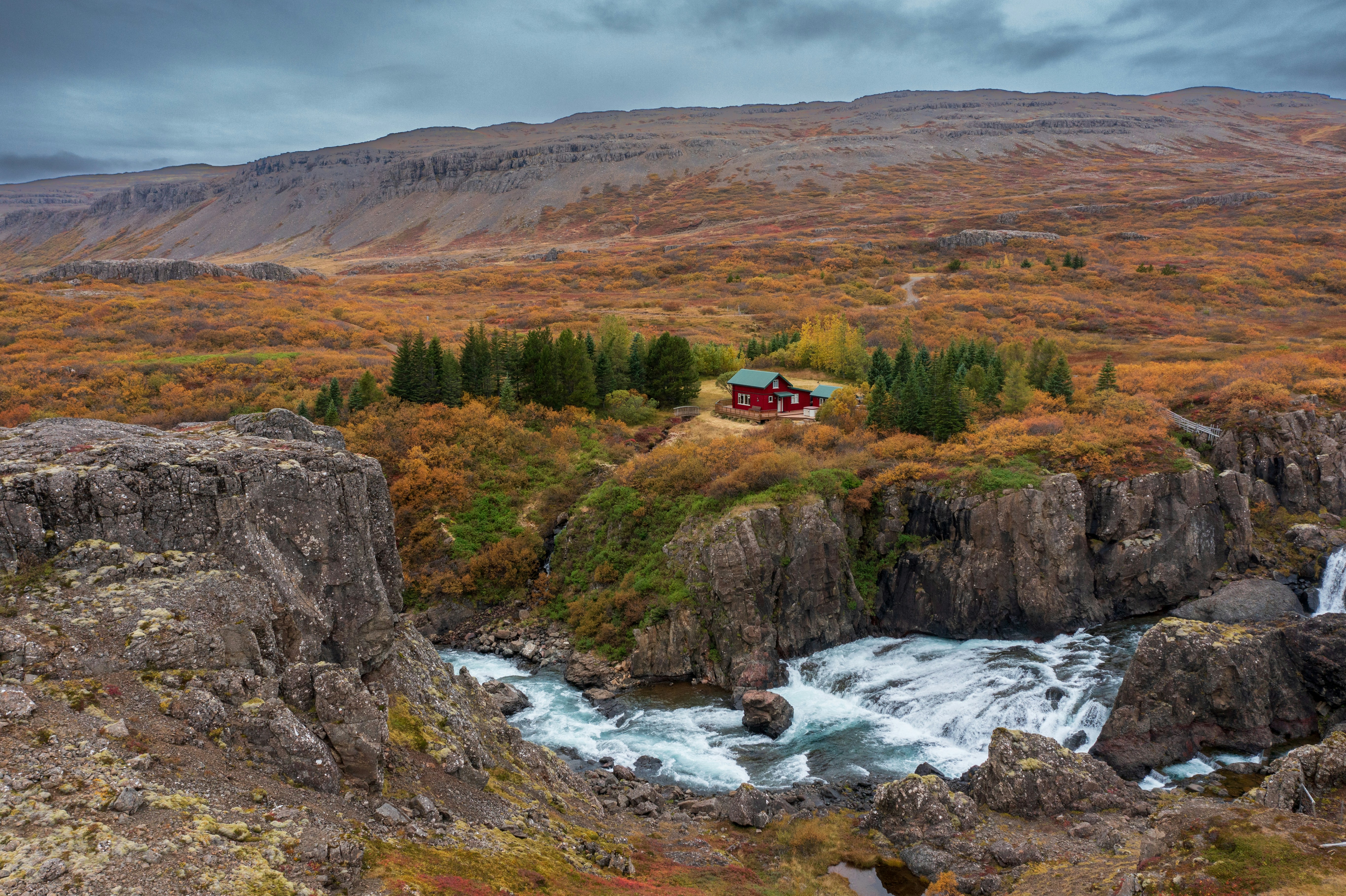 A red-roofed Icelandic farmhouse beside a waterfall, surrounded by autumn foliage
