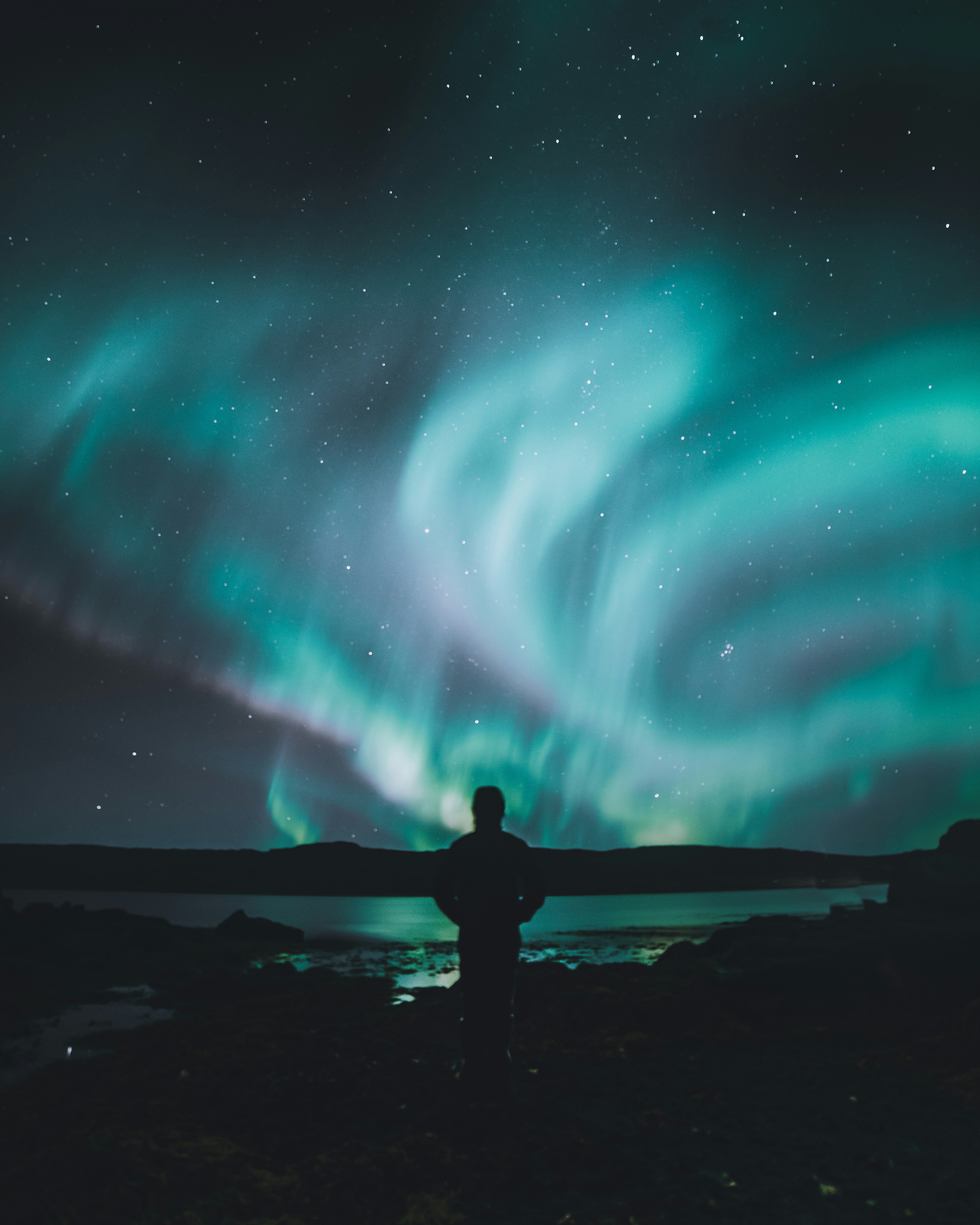 Person standing under a dramatic aurora display in Iceland